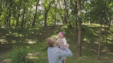 Aile ile çocuk parkta yürüyor. Güneşli bir gün. Yeşil ağaçlar