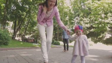 Aile ile çocuk parkta yürüyor. Güneşli bir gün. Yeşil ağaçlar