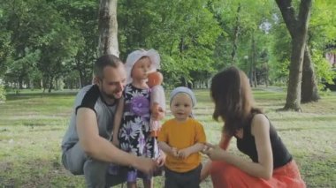Aile ile çocuk parkta yürüyor. Güneşli bir gün. Yeşil ağaçlar