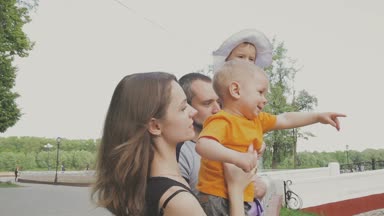 Aile ile çocuk parkta yürüyor. Güneşli bir gün. Yeşil ağaçlar