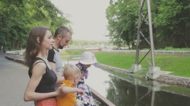 Aile ile çocuk parkta yürüyor. Güneşli bir gün. Yeşil ağaçlar