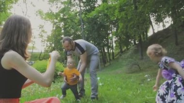 Aile ile çocuk parkta yürüyor. Güneşli bir gün. Yeşil ağaçlar