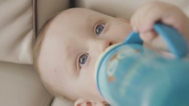 Küçük bir çocuk, bir şişe süt içiyor. Aile evde