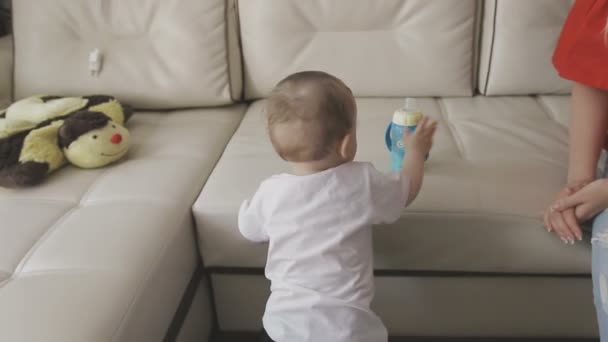 Маленький ребёнок пьёт молоко из бутылки. Семья на дому — стоковое видео