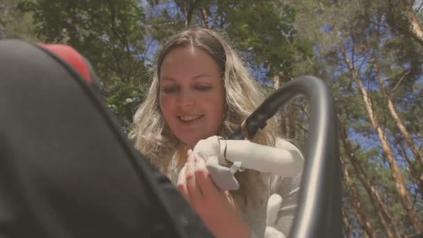 Beautiful woman walking with her little daughter and pushing stroller in park — Stock Video