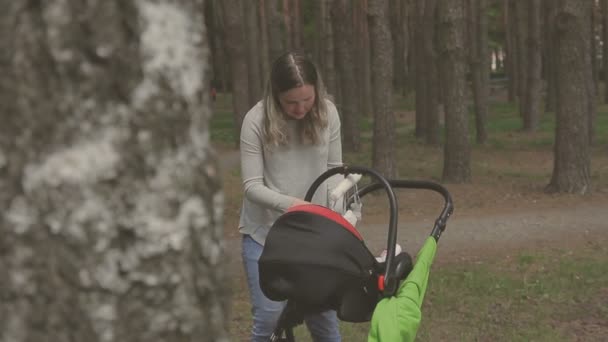 Belle femme marchant avec sa petite fille et poussant poussette dans le parc — Video