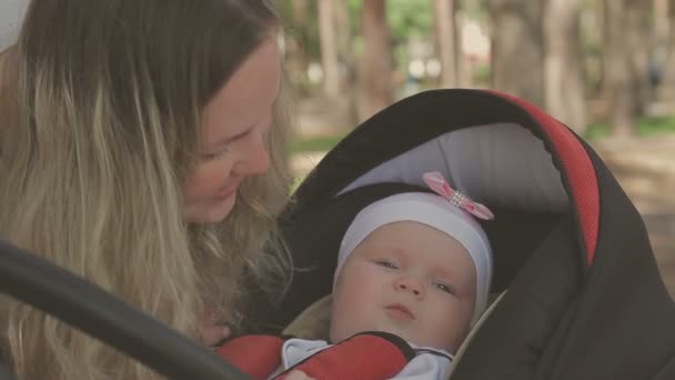 Vacker kvinna promenader med sin lilla dotter och driver sittvagn i park — Stockvideo