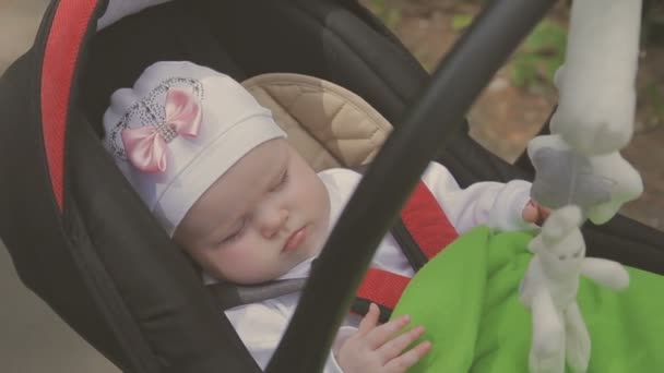 Beautiful woman walking with her little daughter and pushing stroller in park — Stock Video