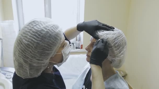 Uma funcionária de uma clínica de cosmetologia faz marcação antes do procedimento de microjateamento — Vídeo de Stock