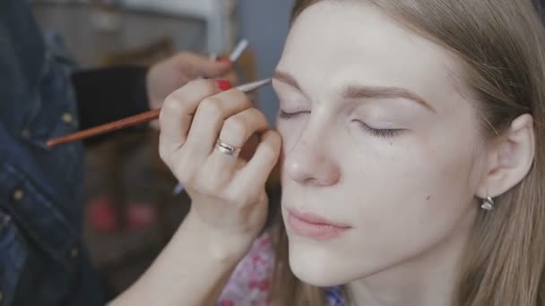 Maquiagem artista faz uma maquiagem profissional para uma menina muito bonita em um estúdio de fotos — Vídeo de Stock