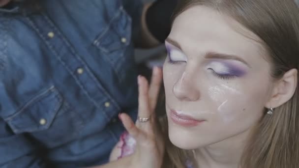 Maquiagem artista faz uma maquiagem profissional para uma menina muito bonita em um estúdio de fotos — Vídeo de Stock