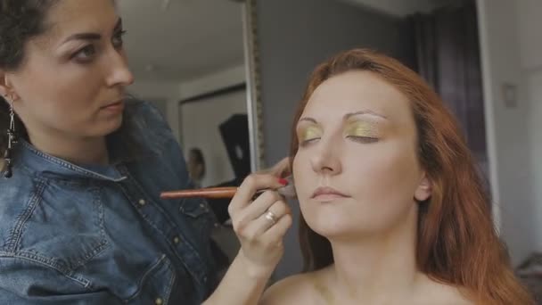 Visagist maakt een professionele make-up voor een heel mooi meisje in een fotostudio — Stockvideo