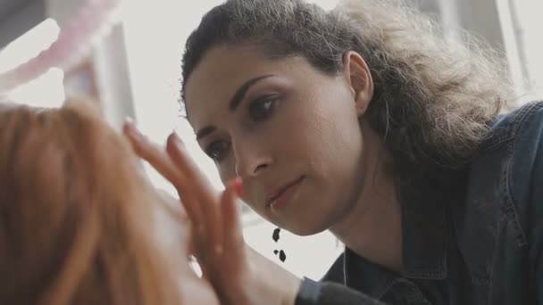 Maquillaje artista hace un maquillaje profesional para una chica muy hermosa en un estudio de fotografía — Vídeo de stock