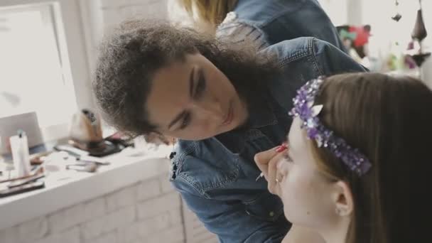 Maquillaje artista hace un maquillaje profesional para una chica muy hermosa en un estudio de fotografía — Vídeo de stock