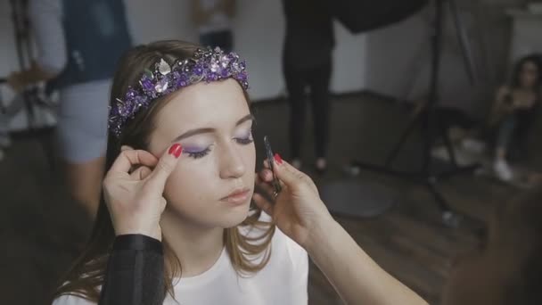 Make-up artist gör en professionell make-up för en mycket vacker flicka i en fotostudio — Stockvideo