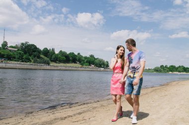 Genç çift, sarılma ve nehir kıyısında birbirlerine gülümsüyor. Kumlu sahilde yürüyüş