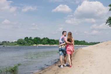 Genç çift, sarılma ve nehir kıyısında birbirlerine gülümsüyor. Kumlu sahilde yürüyüş