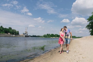 Genç çift, sarılma ve nehir kıyısında birbirlerine gülümsüyor. Kumlu sahilde yürüyüş