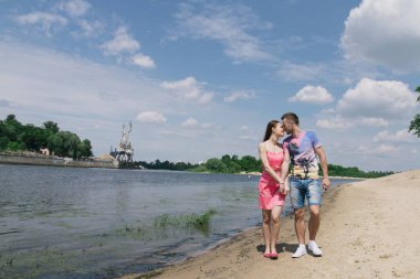 Genç çift, sarılma ve nehir kıyısında birbirlerine gülümsüyor. Kumlu sahilde yürüyüş