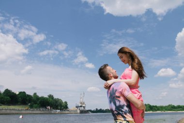 Genç çift, sarılma ve nehir kıyısında birbirlerine gülümsüyor. Kumlu sahilde yürüyüş
