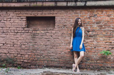 Çok güzel ve neşeli bir kız bir tuğla duvar yakınında sokakta duruyor