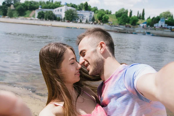 Giovani coppie che si abbracciano e si sorridono sulla riva del fiume. Passeggiando lungo la spiaggia sabbiosa. Crea selfie — Foto Stock