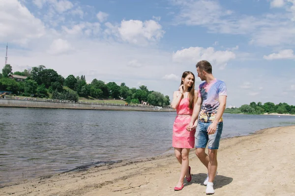 Genç çift, sarılma ve nehir kıyısında birbirlerine gülümsüyor. Kumlu sahilde yürüyüş