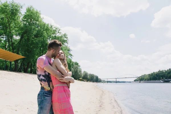 Jong (echt) paar knuffelen en glimlachen naar elkaar op de rivieroever. Wandelen langs het zandstrand — Stockfoto