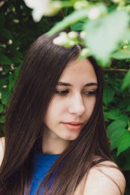 Çok güzel ve neşeli kız beyaz çiçekli bir çalı yakınında sokakta duruyor