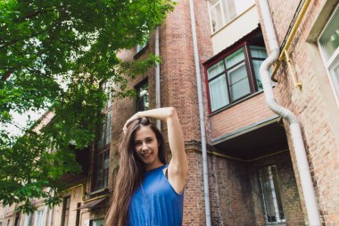 Çok güzel ve neşeli bir kız bir tuğla duvar yakınında sokakta duruyor