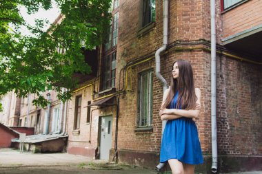 Çok güzel ve neşeli bir kız bir tuğla duvar yakınında sokakta duruyor