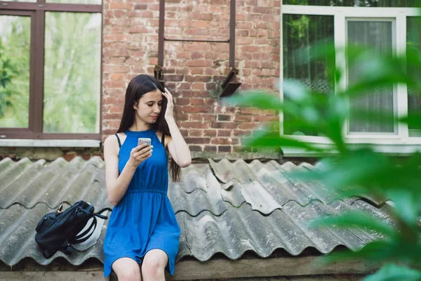 Ένα πολύ όμορφο και χαρούμενο κορίτσι στέκεται στο δρόμο με μακρύς, πολυτελήs μαλλιά και κάθεται με το τηλέφωνό της — Φωτογραφία Αρχείου