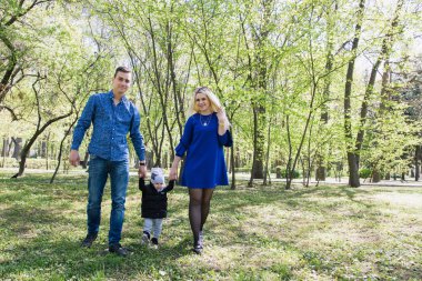 Mutlu genç aile dışarıda yeşil doğada birlikte vakit geçiriyor.