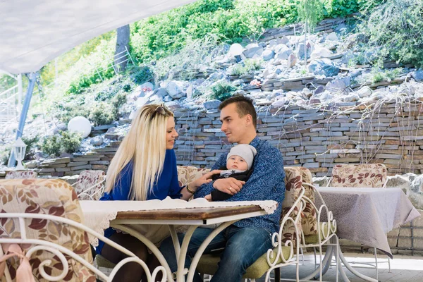 Una feliz pareja de casados está sentada en un café y disfrutando de este tiempo. Juegan con su hijo, él sonríe . —  Fotos de Stock