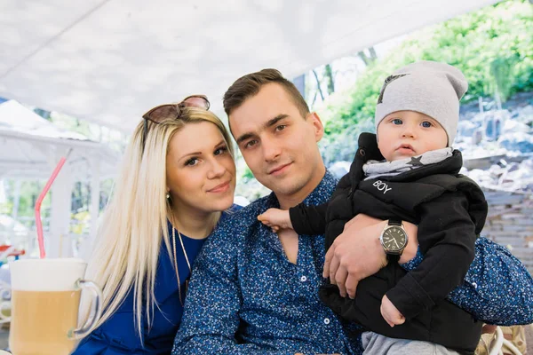 Una feliz pareja de casados está sentada en un café y disfrutando de este tiempo. Juegan con su hijo, él sonríe . — Foto de Stock