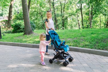 Parkta bir bebek arabası itme sırasında yürüyüş anne