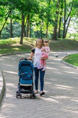 Parkta bir bebek arabası itme sırasında yürüyüş anne