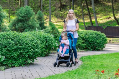 Parkta bir bebek arabası itme sırasında yürüyüş anne