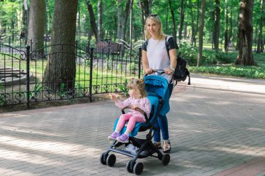 Parkta bir bebek arabası itme sırasında yürüyüş anne