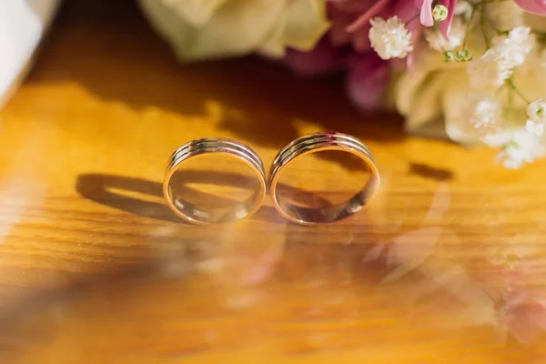 Bella immagine tonica con fedi nuziali si trovano su una superficie di legno sullo sfondo di un mazzo di fiori. — Foto Stock