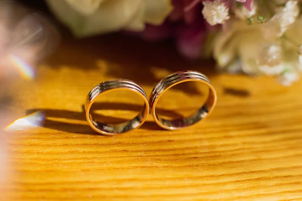 Imagem tonificada bonita com anéis de casamento jazem em uma superfície de madeira contra o fundo de um buquê de flores. — Fotografia de Stock