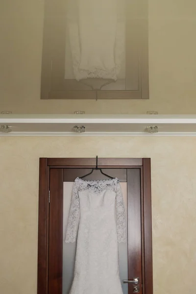 Vestido de novia colgado en una puerta de madera en una habitación luminosa . —  Fotos de Stock