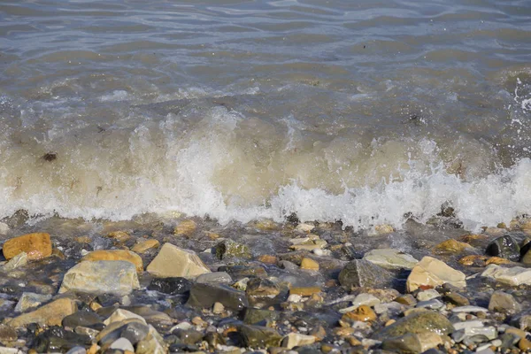 çakıl plaj çakıl deniz ve güneşin ışınları tarafından aydınlatılan su dalgaları üzerinde.