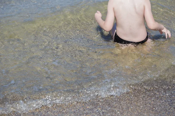 少年は海の水で背中を座っています。. — ストック写真