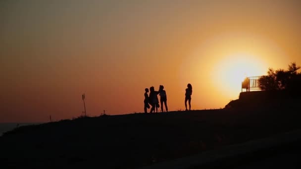 Siluetter av vänner som står på en klippa i solnedgången. — Stockvideo