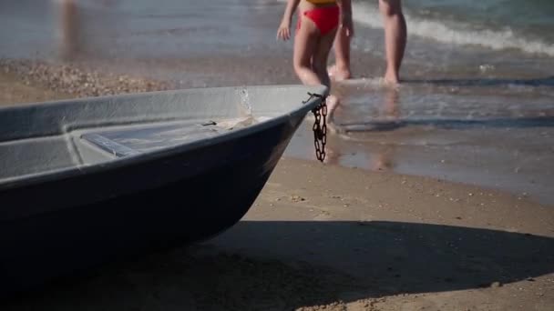 Um velho barco de pesca fica na praia junto ao mar, onde as pessoas caminham . — Vídeo de Stock