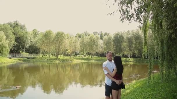 Los amantes de pie en la orilla del lago hablando abrazo y beso . — Vídeo de stock
