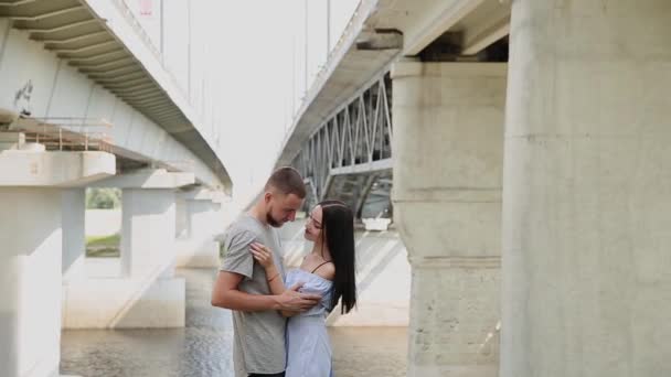 Un couple aimant se tient sous un pont étreignant et embrassant . — Video