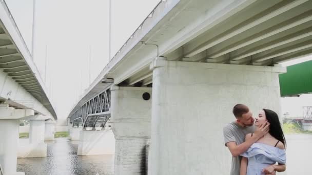 Ein liebendes Paar steht unter einer Brücke und umarmt und küsst sich. — Stockvideo