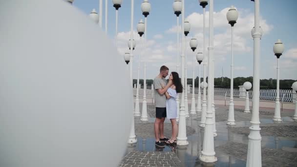 Una pareja cariñosa abraza y besa en el terraplén cerca de las farolas . — Vídeo de stock